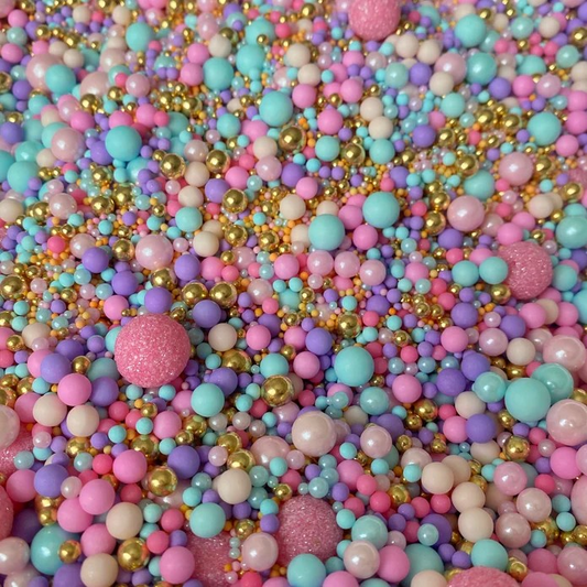 A variety of colorful edible baking decorations (sprinkles), including purple pearls and gold beads, mixed together.